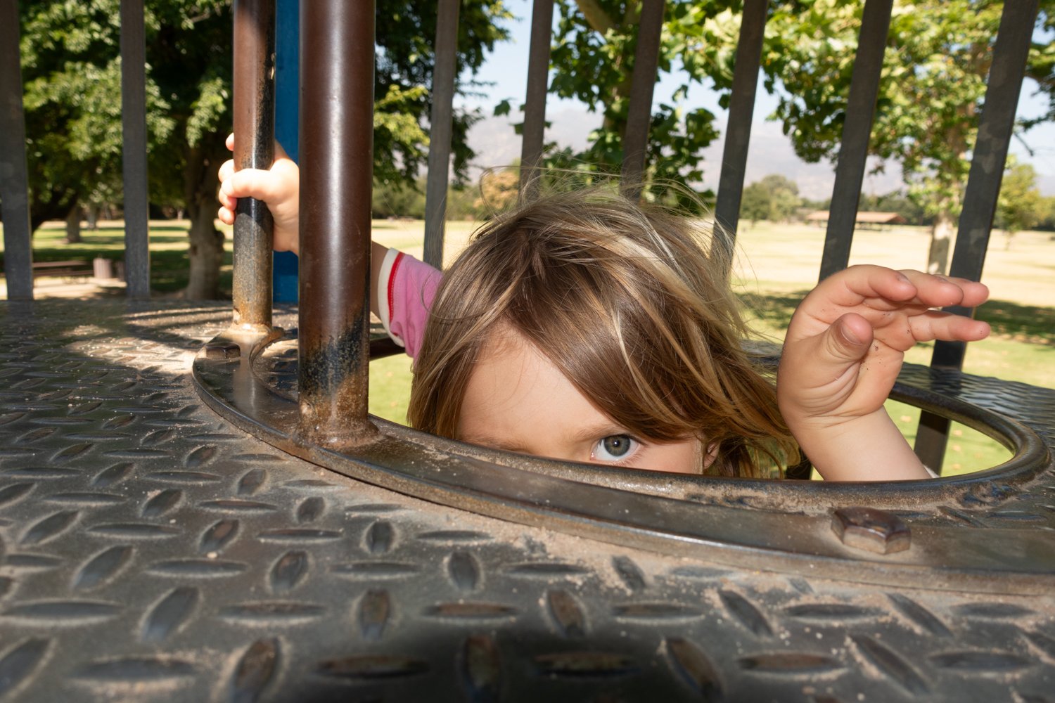 A child plays on a playground in Ojai, California, peeking through the opening of the play structure.