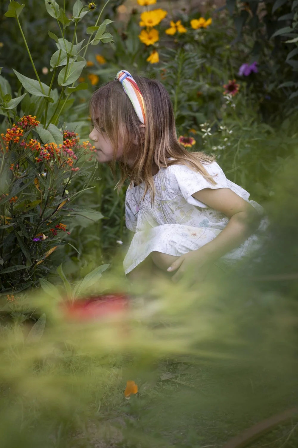 A young girl explores a colorful garden surrounded by flowers and greenery.