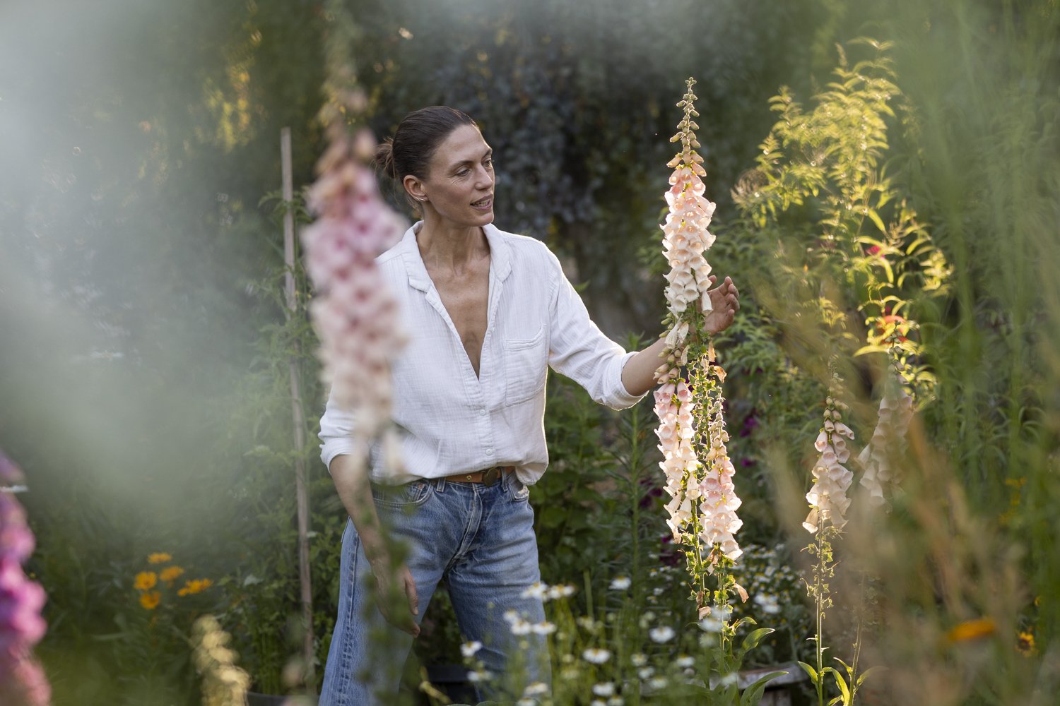 A woman walks through a garden surrounded by tall flowers and plants.