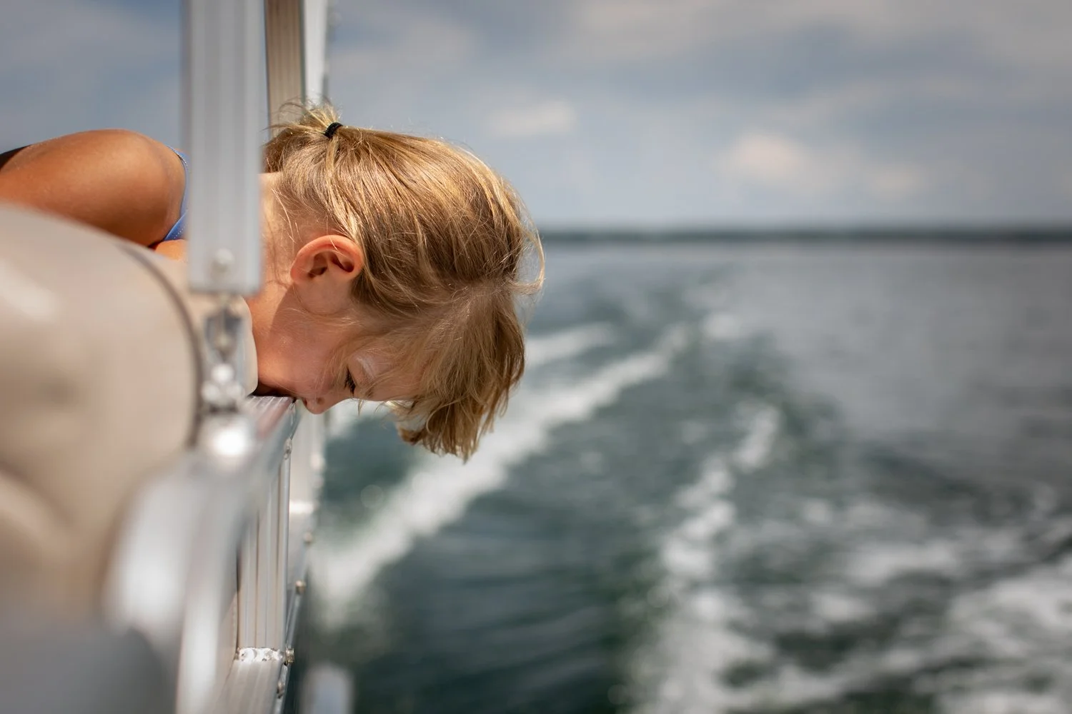 A child leans over the side of a boat looking out at the water.