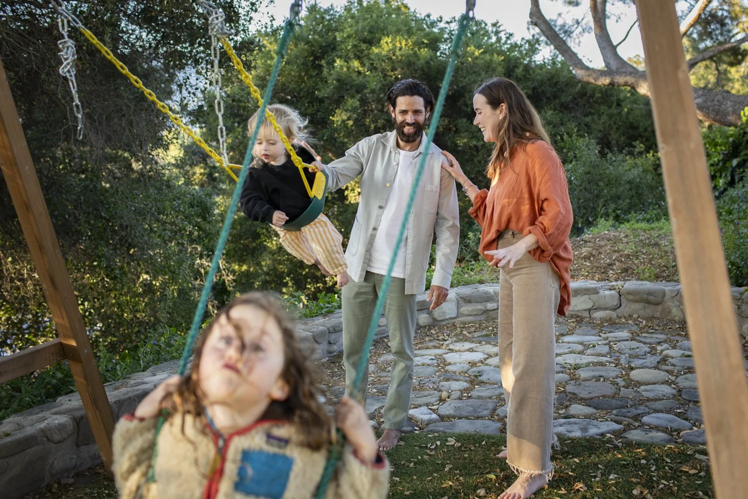 A family plays together outdoors on a swing in their garden.