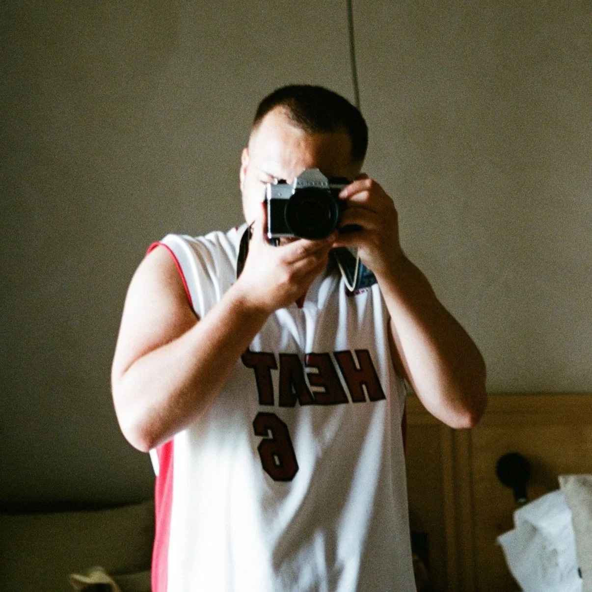 Person taking a photo with a camera, wearing a basketball jersey.