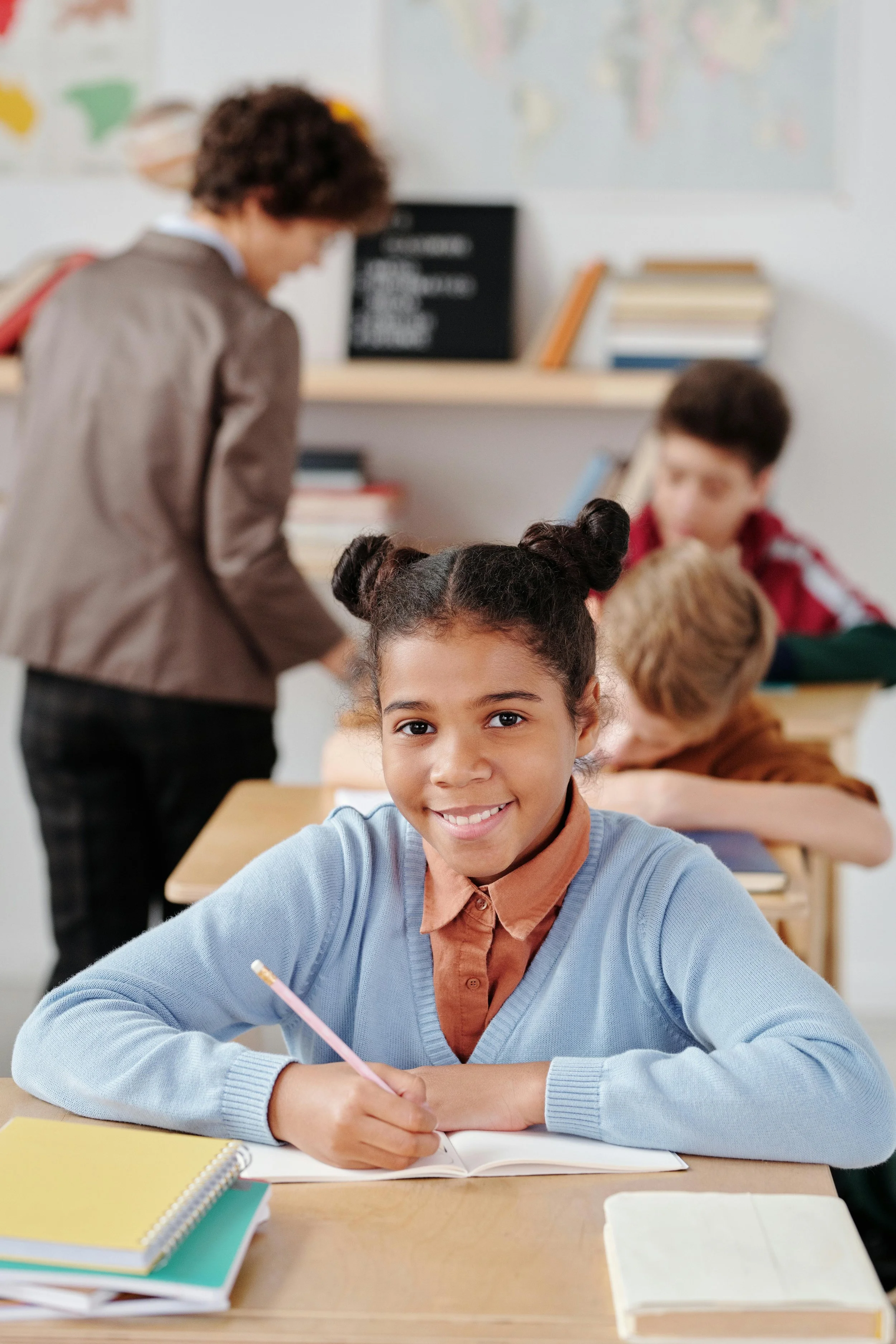 child sits at desk holding pencil and smiling