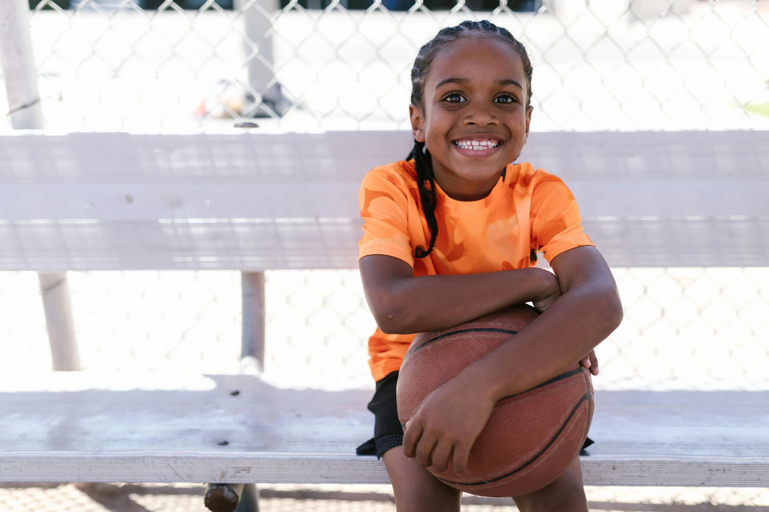 child sits on bench holding basketball and smiling