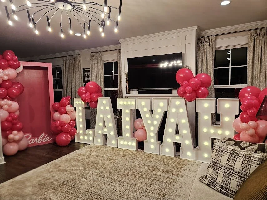 Decorative balloon arrangement with pink, cream, green, and gold balloons along a staircase railing.