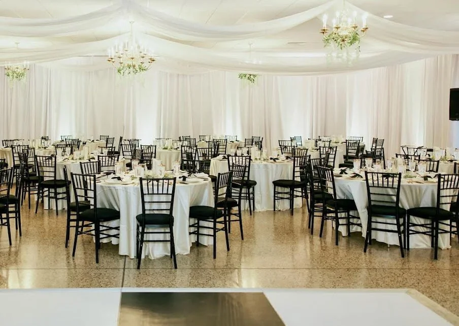 Elegant banquet hall with round tables covered in white tablecloths, black chairs, and chandeliers