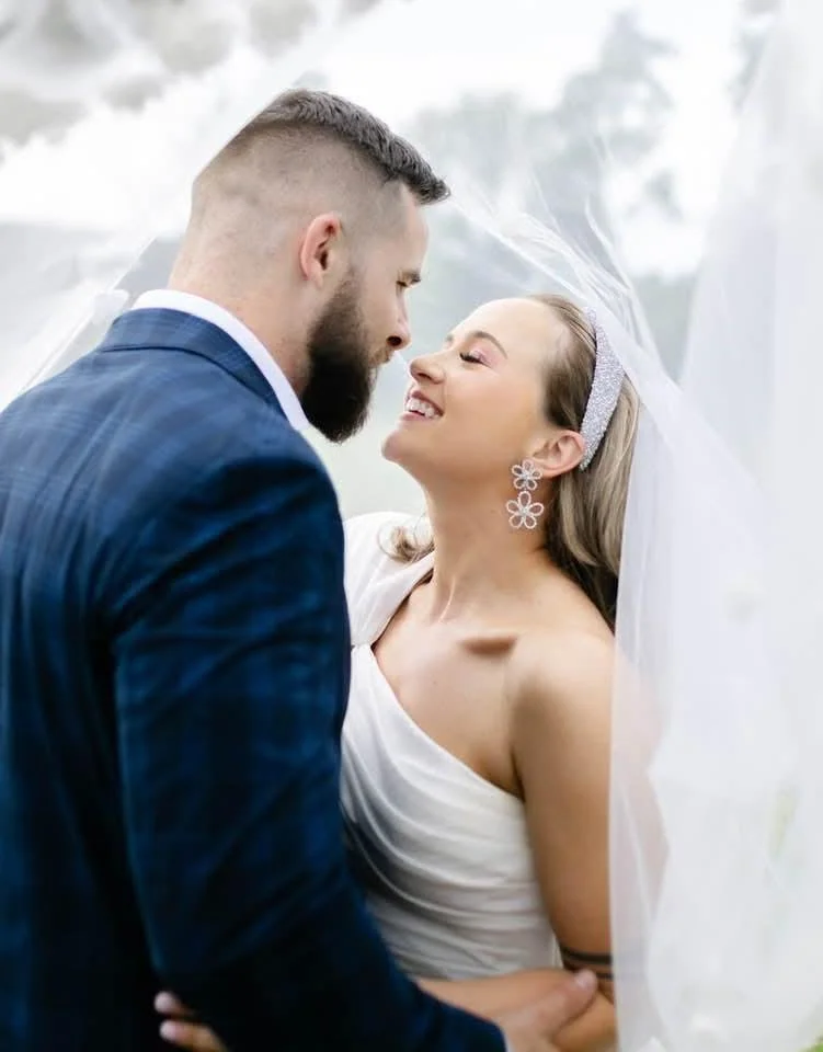 A bride and groom are standing close together, smiling, with the bride looking up at the groom and the groom looking down at her, during their wedding.