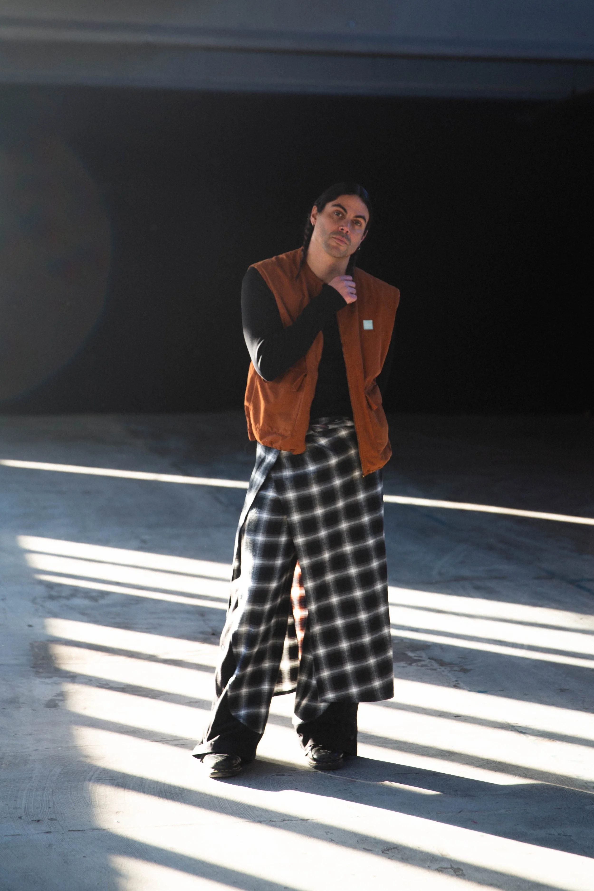 Alex Vargas standing in a dimly lit space with sunlight streaming through slatted openings on the ground.