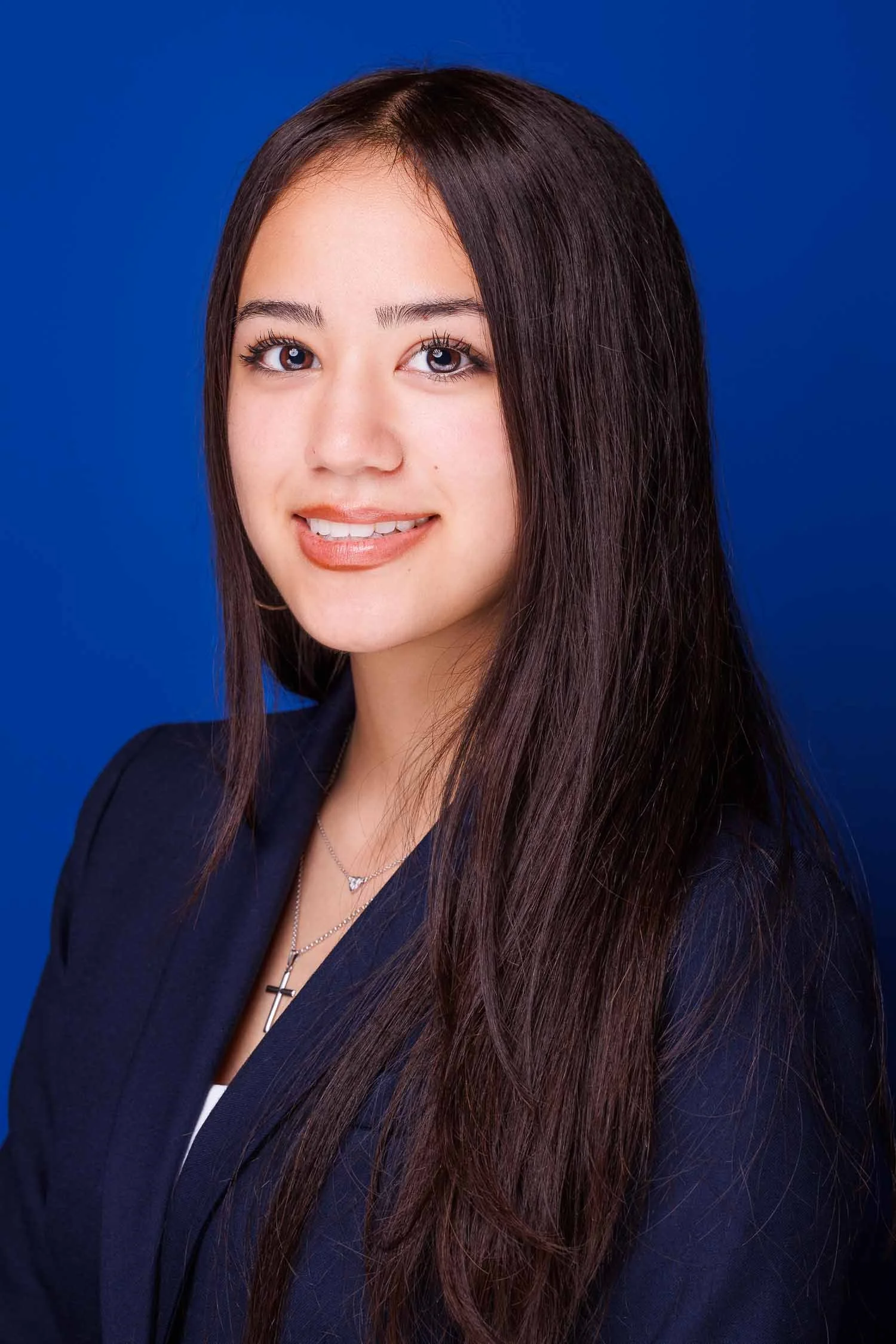 Professional headshot of a young woman in business attire against a blue background photographed by an Orlando headshot photographer, JMC Innovations.