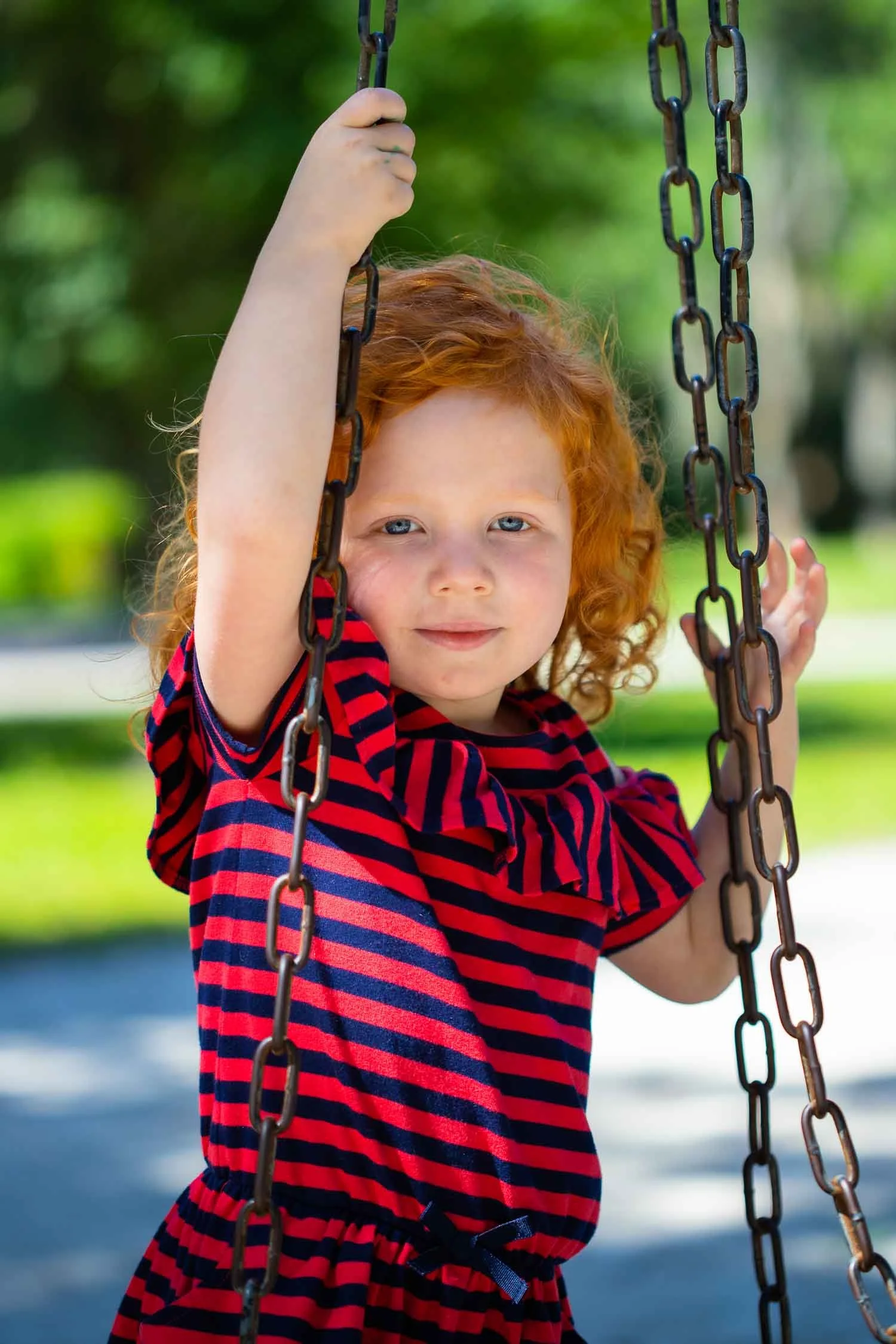 Young red-haired girl standing on playground swings during an outdoor family portrait session photographed by a Tampa family photographer, JMC Innovations.