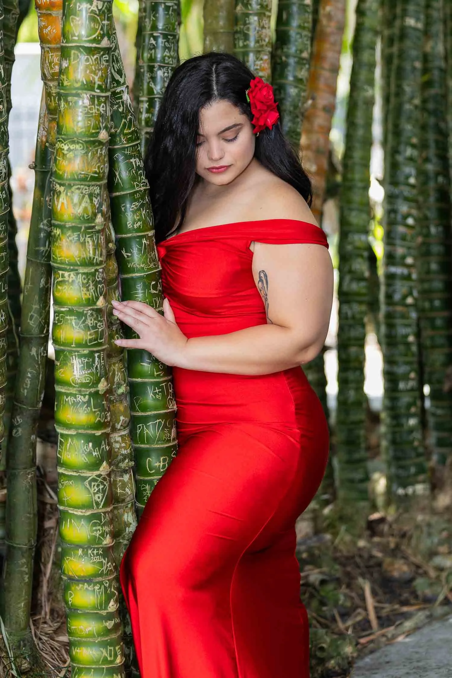 Woman in a flowing red dress posing beside bamboo during an outdoor portrait session photographed by a Lakeland portrait photographer, JMC Innovations.