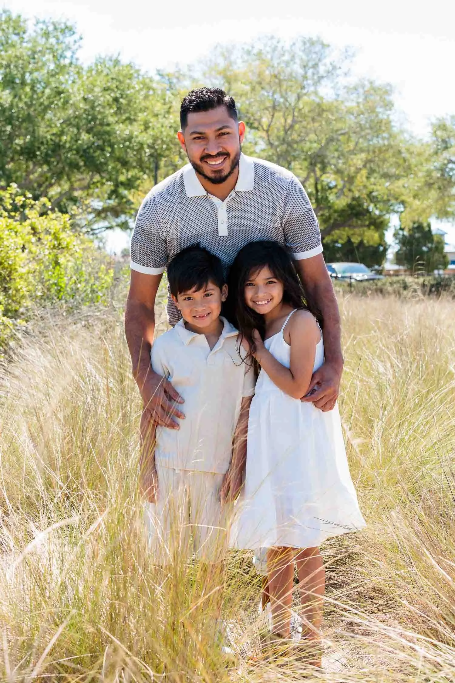 Father posing with his children during an outdoor family portrait session in tall grass photographed by a Tampa family photographer, JMC Innovations.