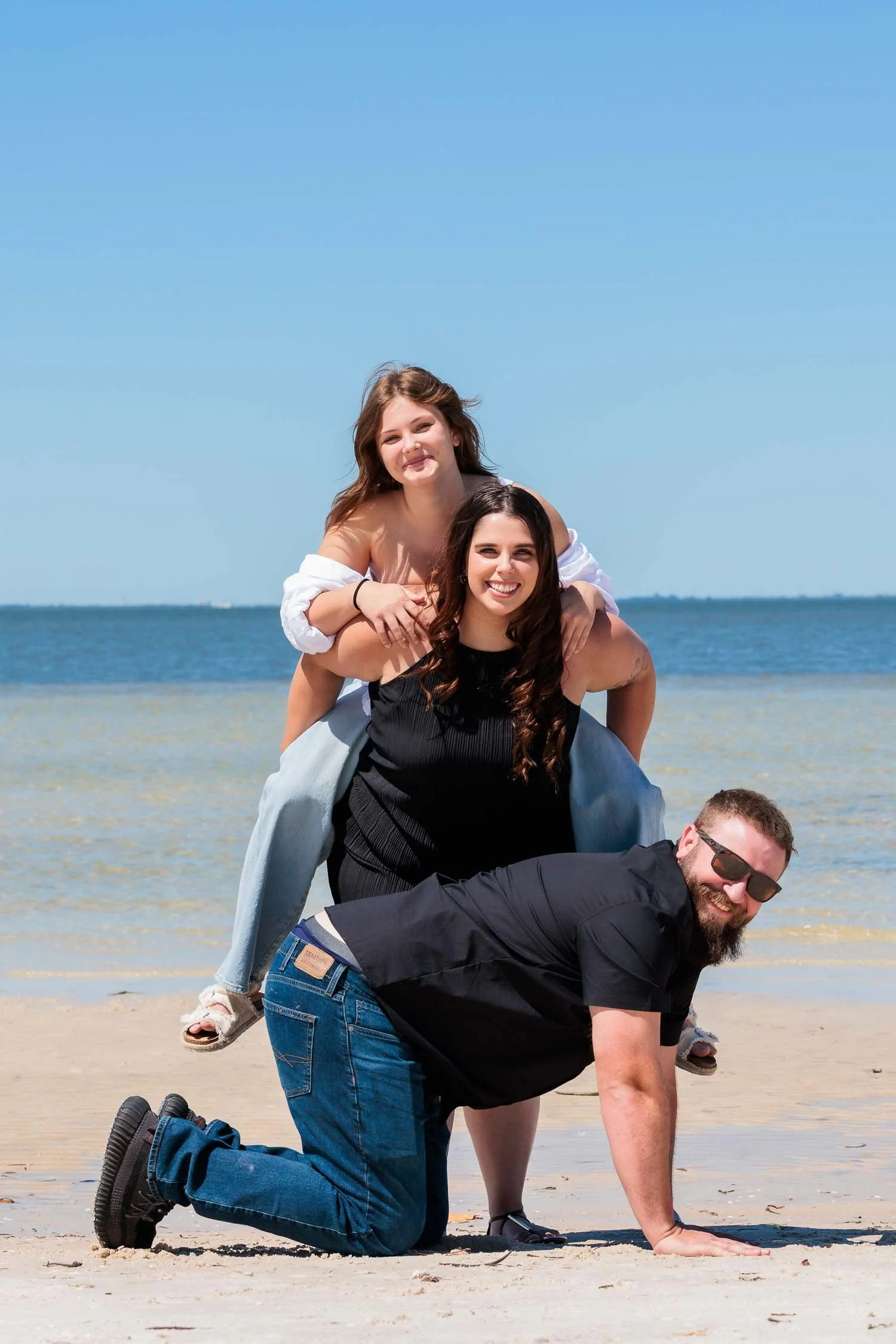 Family posing playfully together on the beach during an outdoor portrait session photographed by a Tampa family photographer, JMC Innovations.
