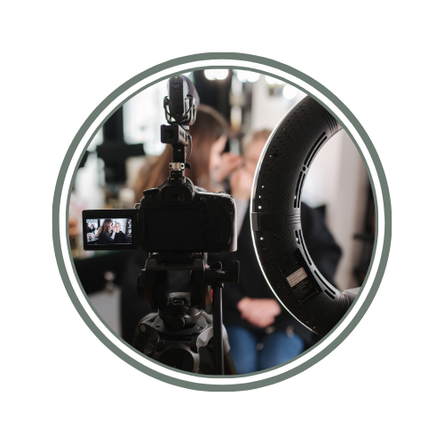 A person being filmed or photographed during a studio shoot with a professional camera and ring light.
