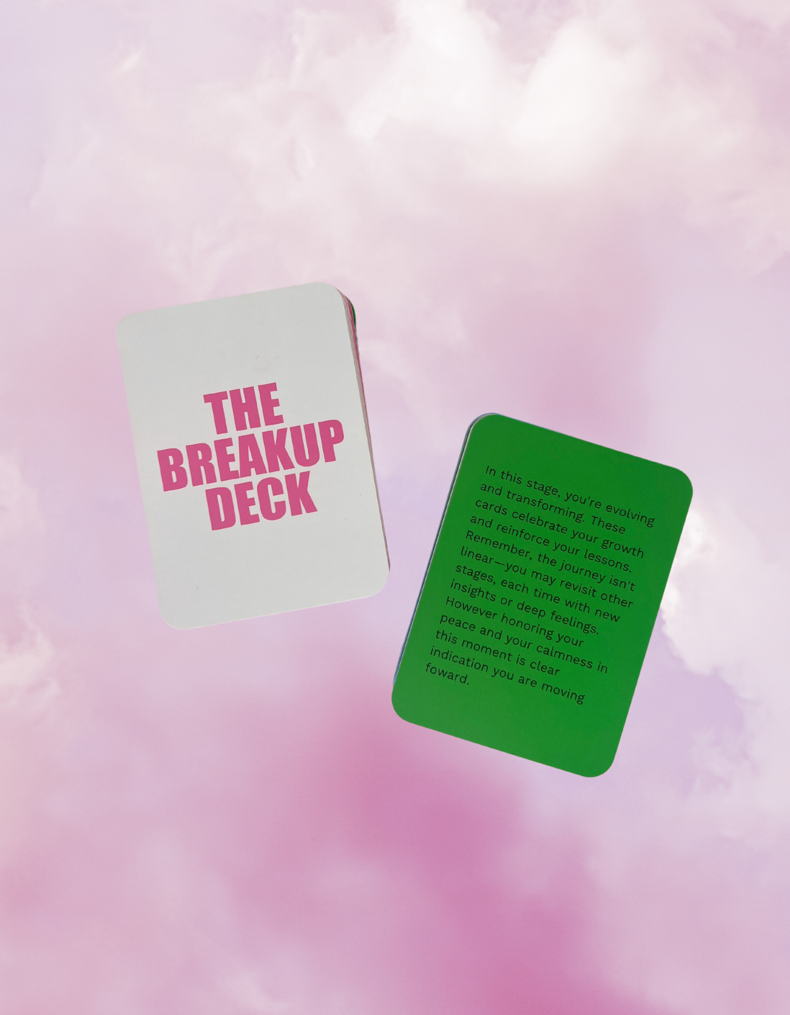 Cards from 'The Breakup Deck' floating against a pink and purple cloudy sky background.