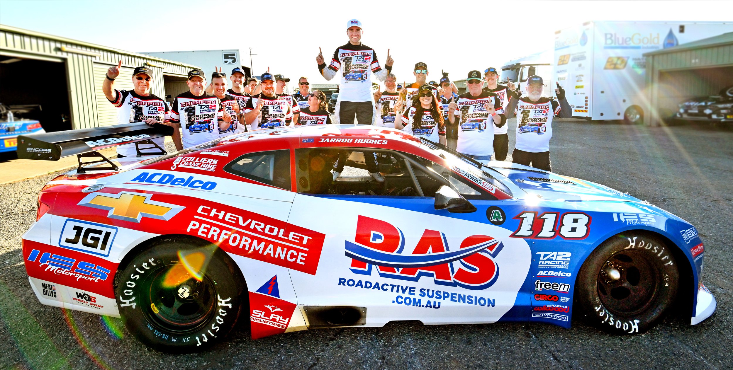 Race car with the number 118 and team members celebrating behind it in a paddock area.