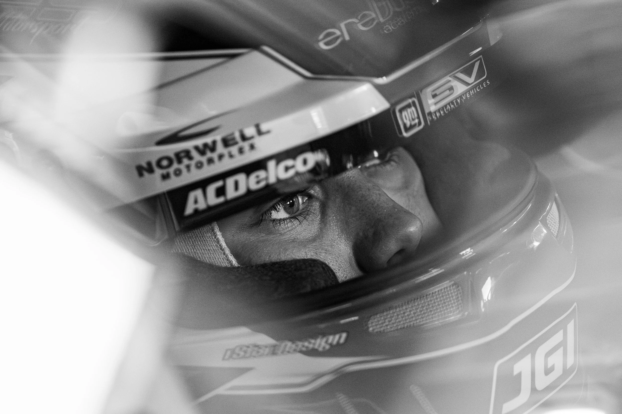 Close-up of a race car driver wearing a helmet, with focus on one eye, in black and white.