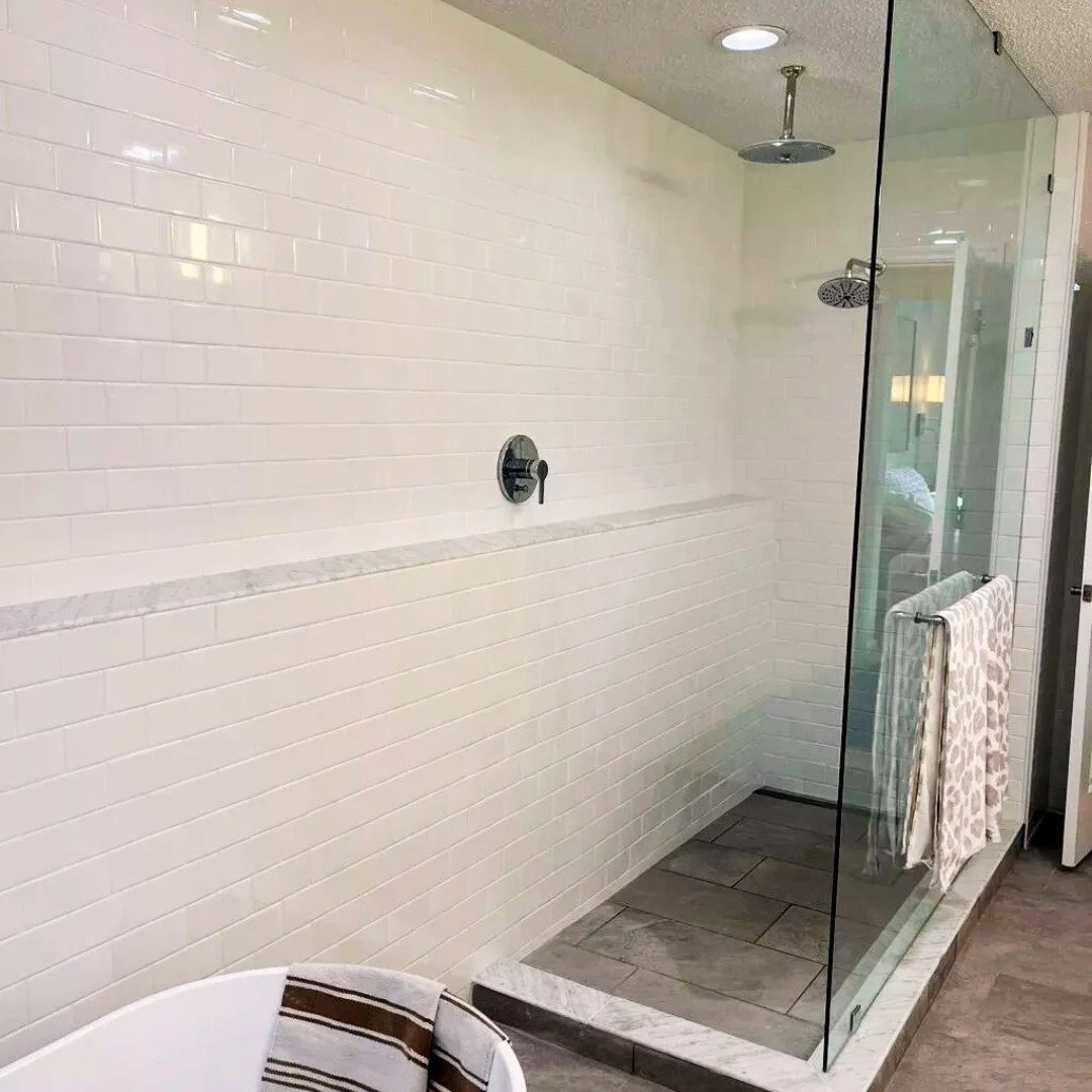 Modern walk-in shower with white subway tile walls, a glass enclosure, two showerheads, a marble shelf, and a towel hanging on the glass panel.