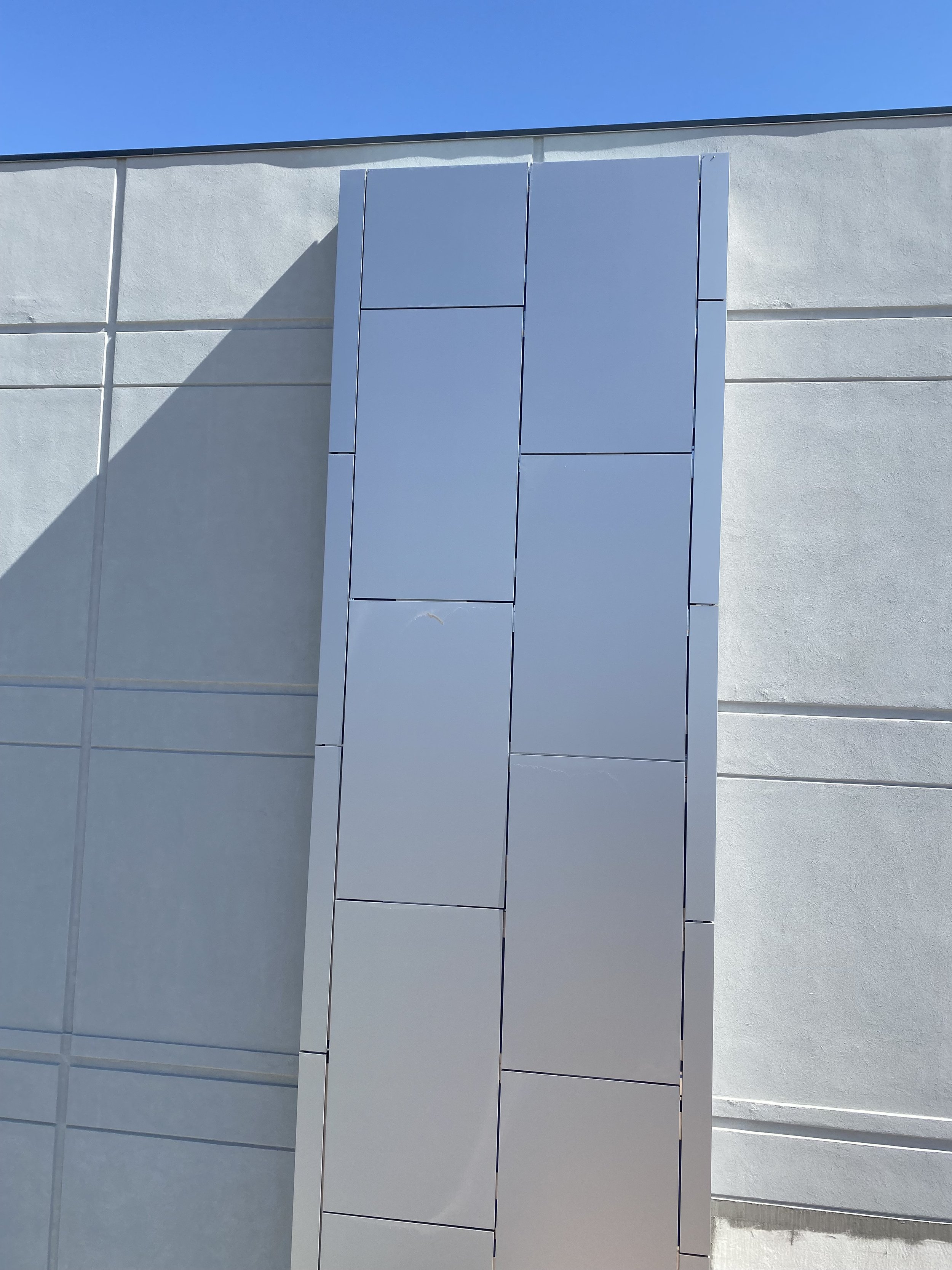 Modern commercial facade with gray vertical sheet metal panels and deep shadow cast under clear blue sky