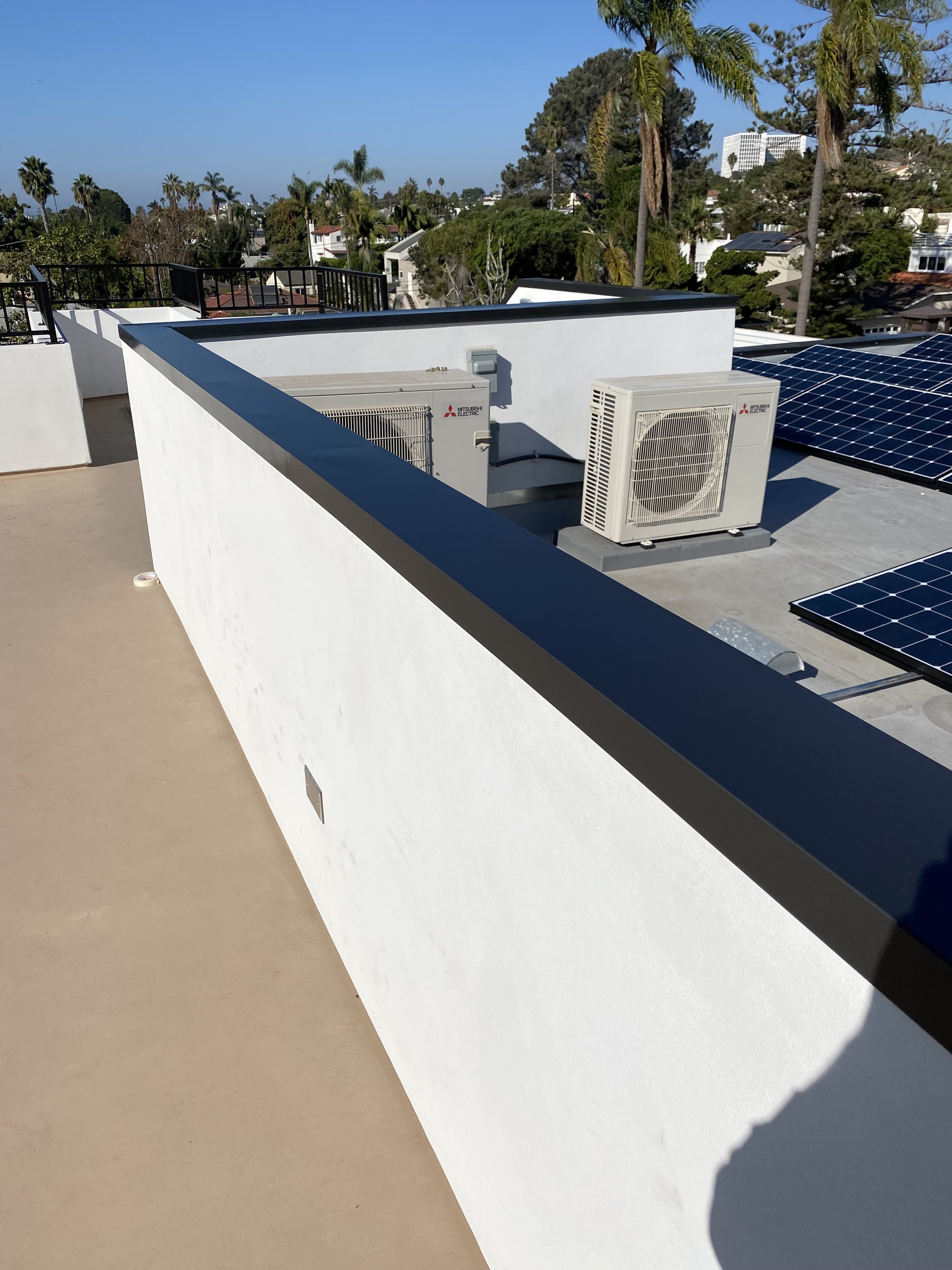 Rooftop setup with solar panels, HVAC units, and parapet wall; urban backdrop with trees and mid-rise buildings visible