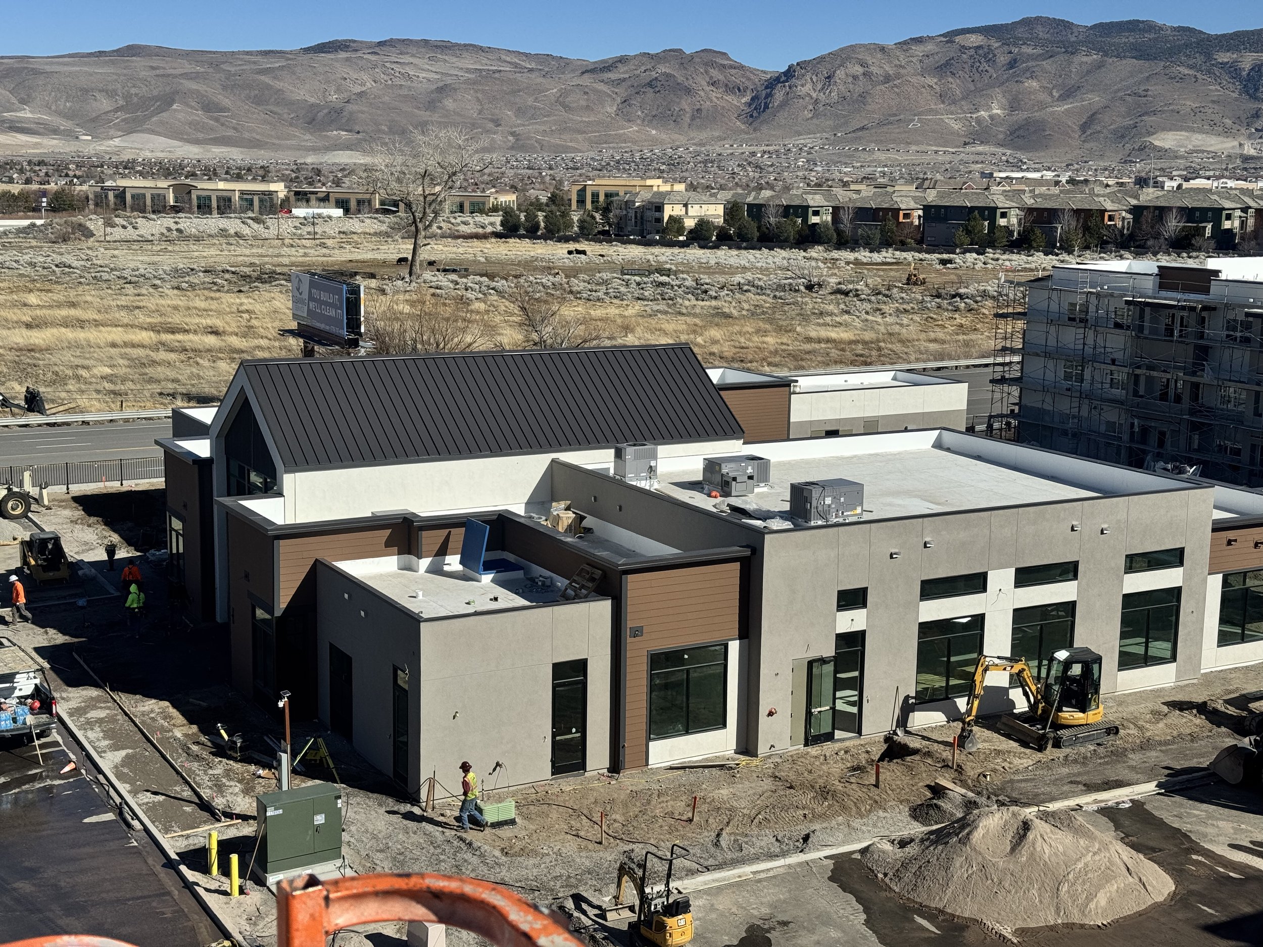 Large-scale construction site with modern building, workers, and equipment in progress against mountainous Southern California backdrop