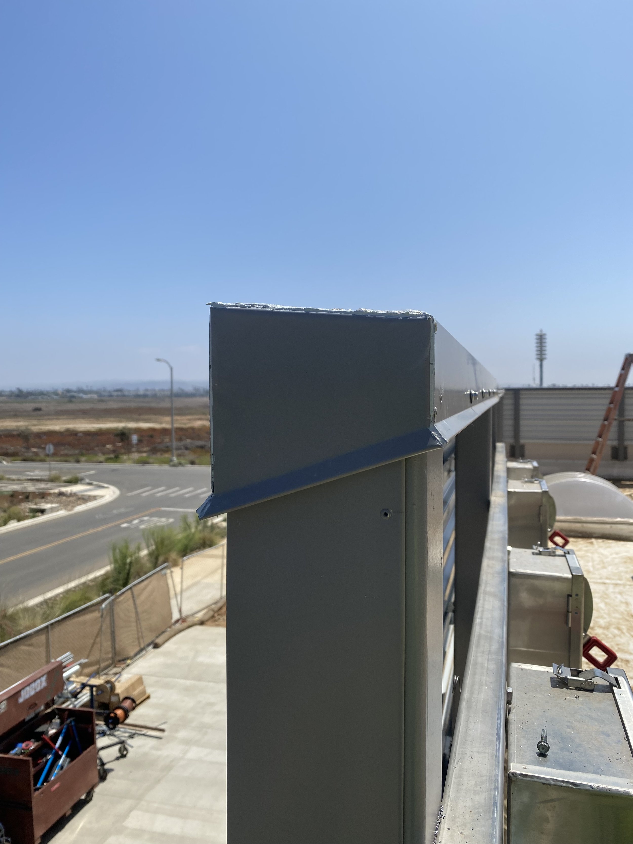 Rooftop view showing installed mechanical enclosures, parapet coping, and sheet metal structures with road in background