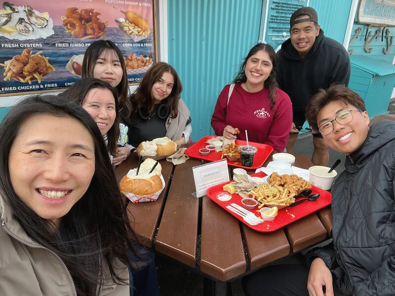 Group of six people sitting around a table at a restaurant, enjoying fried seafood and drinks, smiling for the camera.