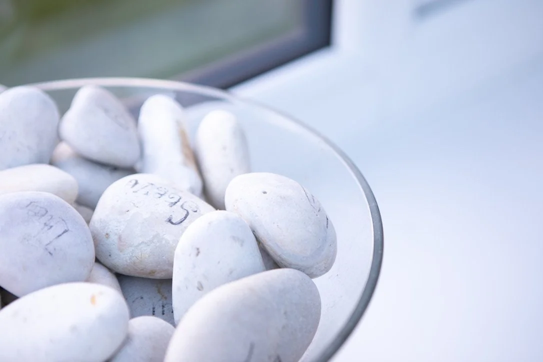 A glass bowl containing white stones sitting near a window on a white surface.