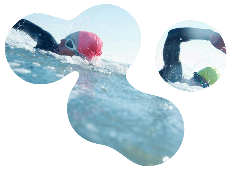Swimmers practicing in an outdoor pool, wearing swim caps and goggles, with one swimmer in a black wetsuit and another in a neon-green swim cap, during daytime.