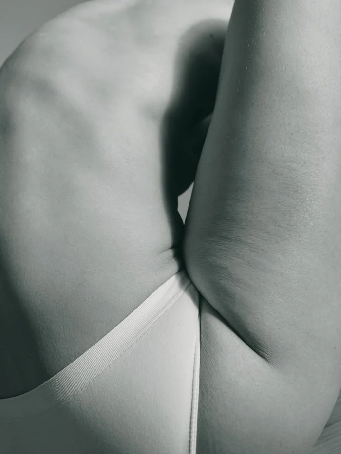Close-up of a nude human body, focusing on the back, with monochrome lighting.