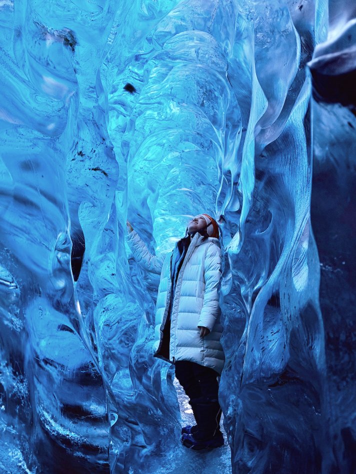 Person wearing a white winter coat exploring inside a blue ice cave.