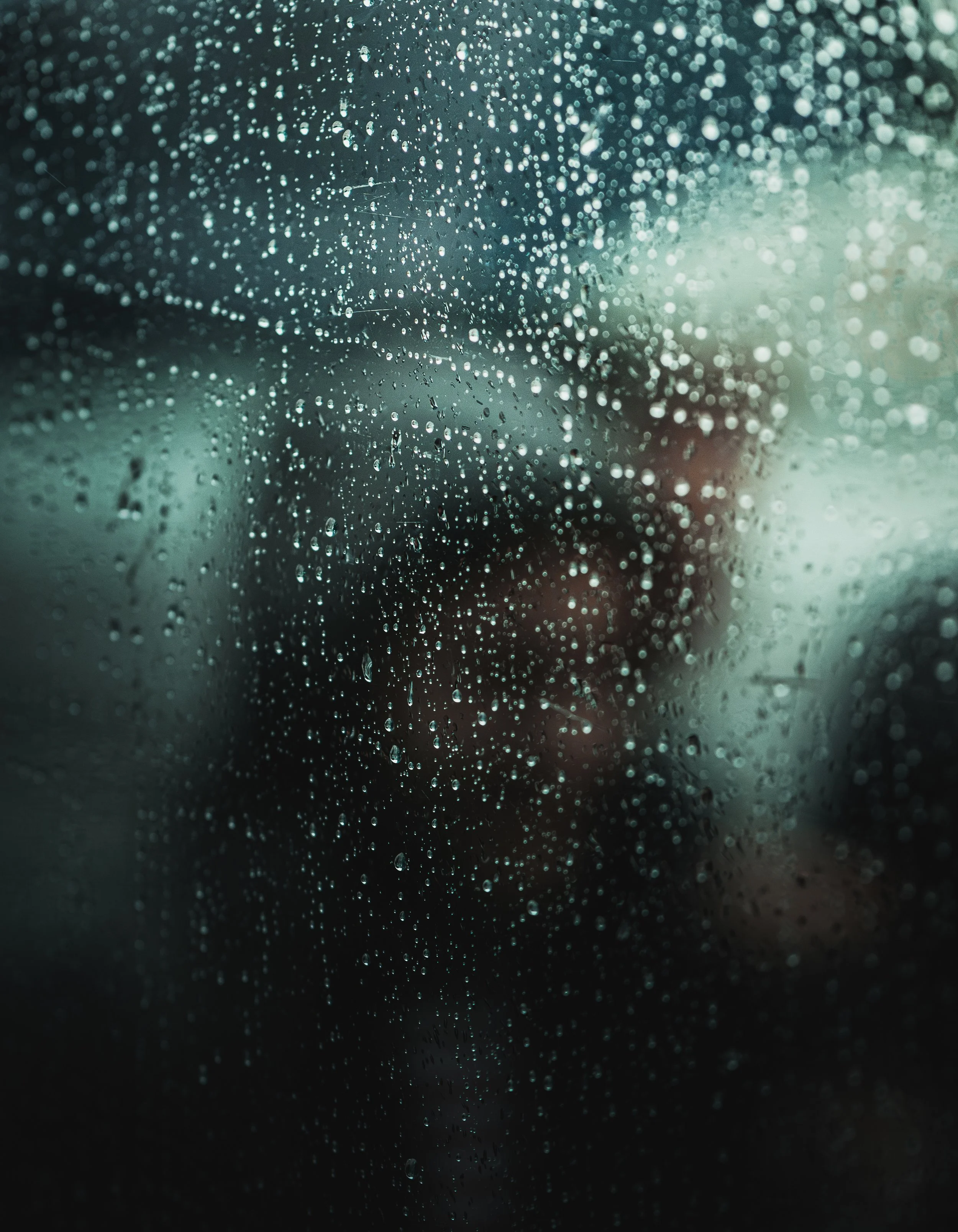 Gouttelettes de pluie sur une fenêtre avec un flou en arrière-plan, probablement une personne.