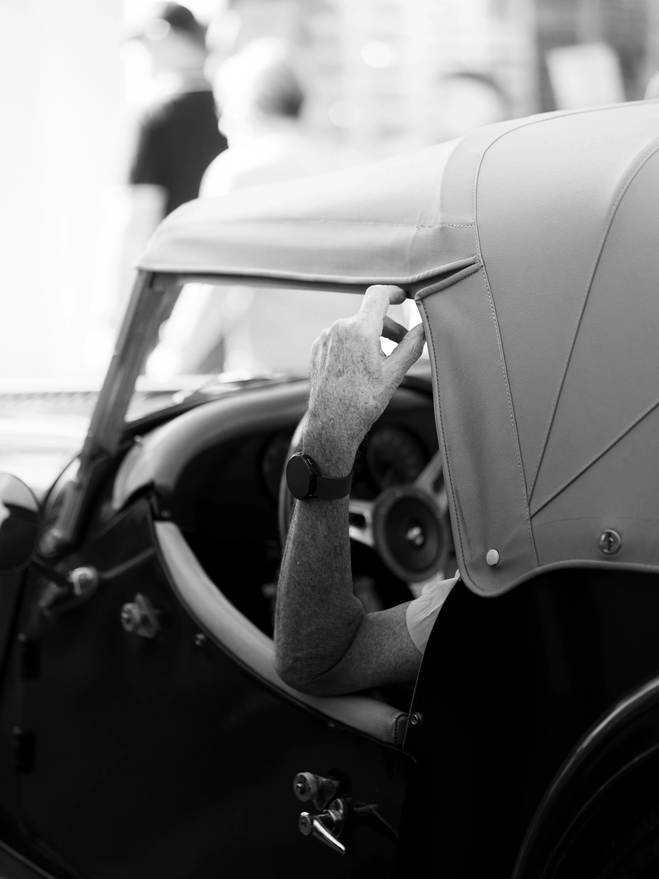 Main d'une personne ajustant la capote d'une voiture de course classique, vue en gros plan en noir et blanc.