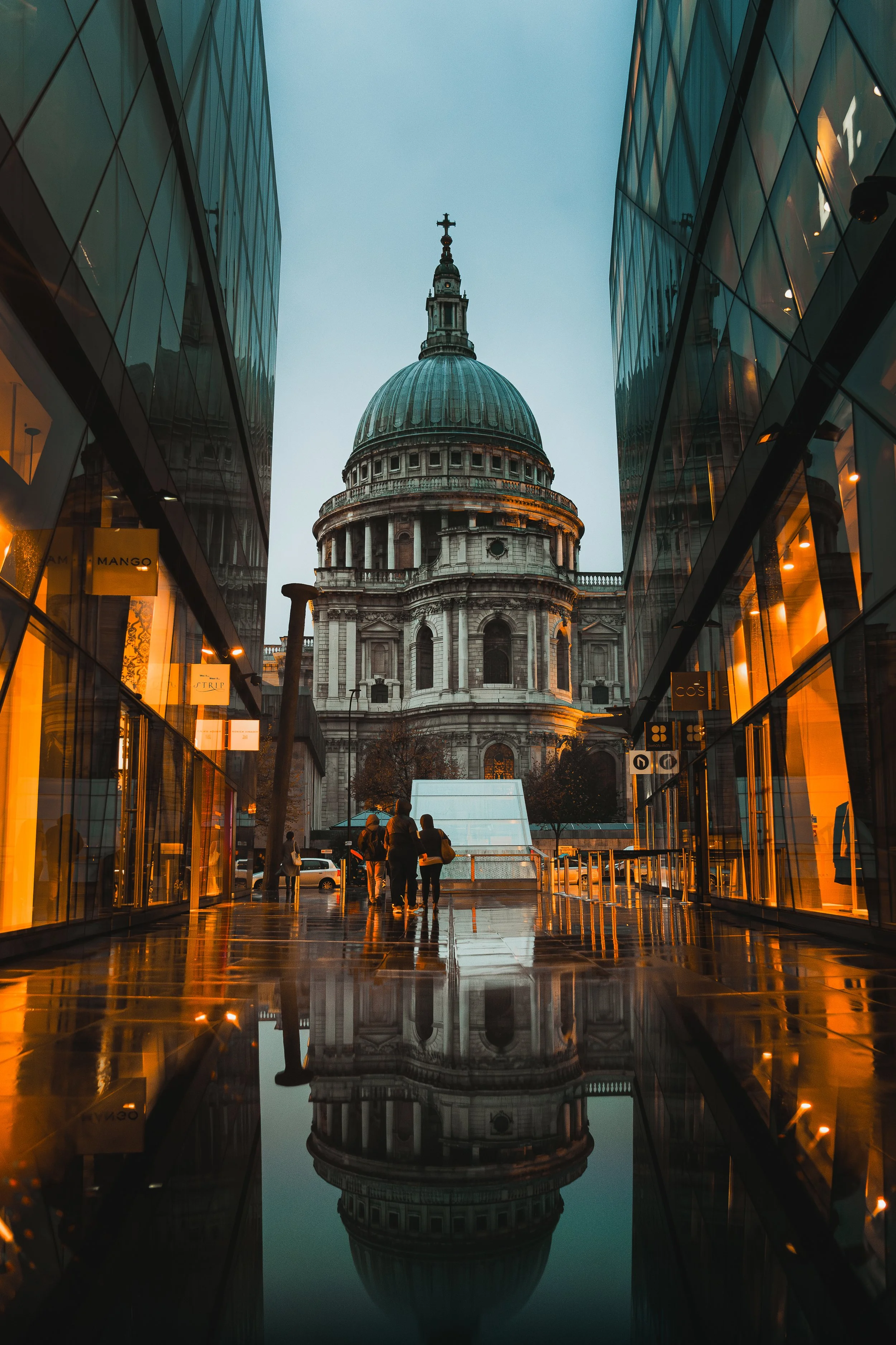 Vue de la cathédrale Saint-Paul de Londres vue entre deux bâtiments modernes, avec une reflection dans une flaque d'eau au sol