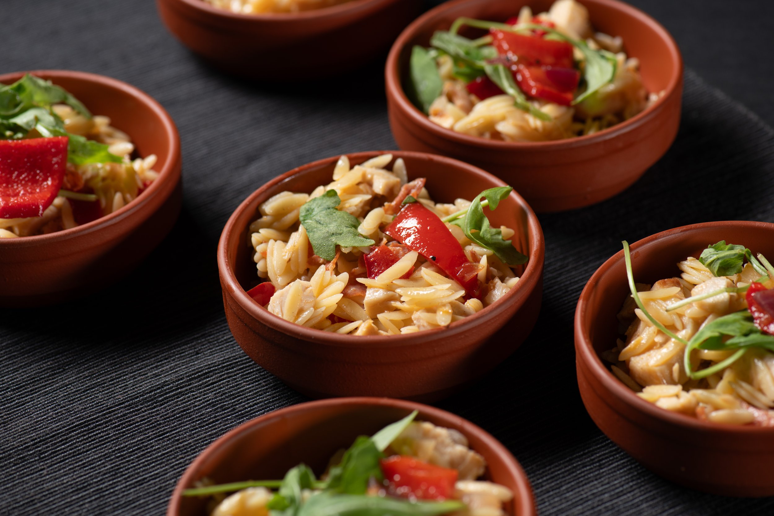 Small bowls of orzo pasta salad with red bell peppers and arugula
