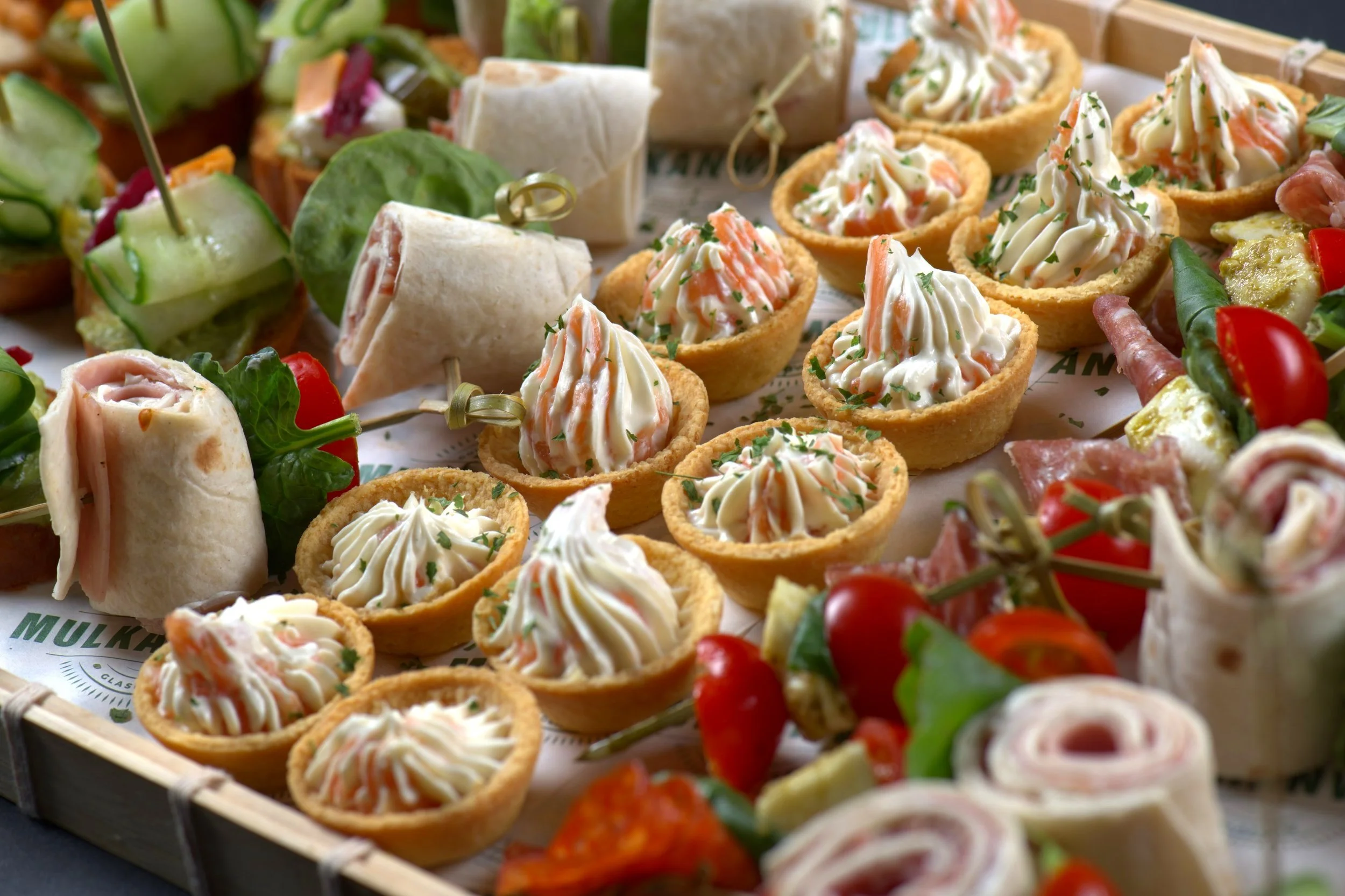 Close-up of assorted appetizers including tortilla wraps, savory tarts with cream, and skewered vegetables.