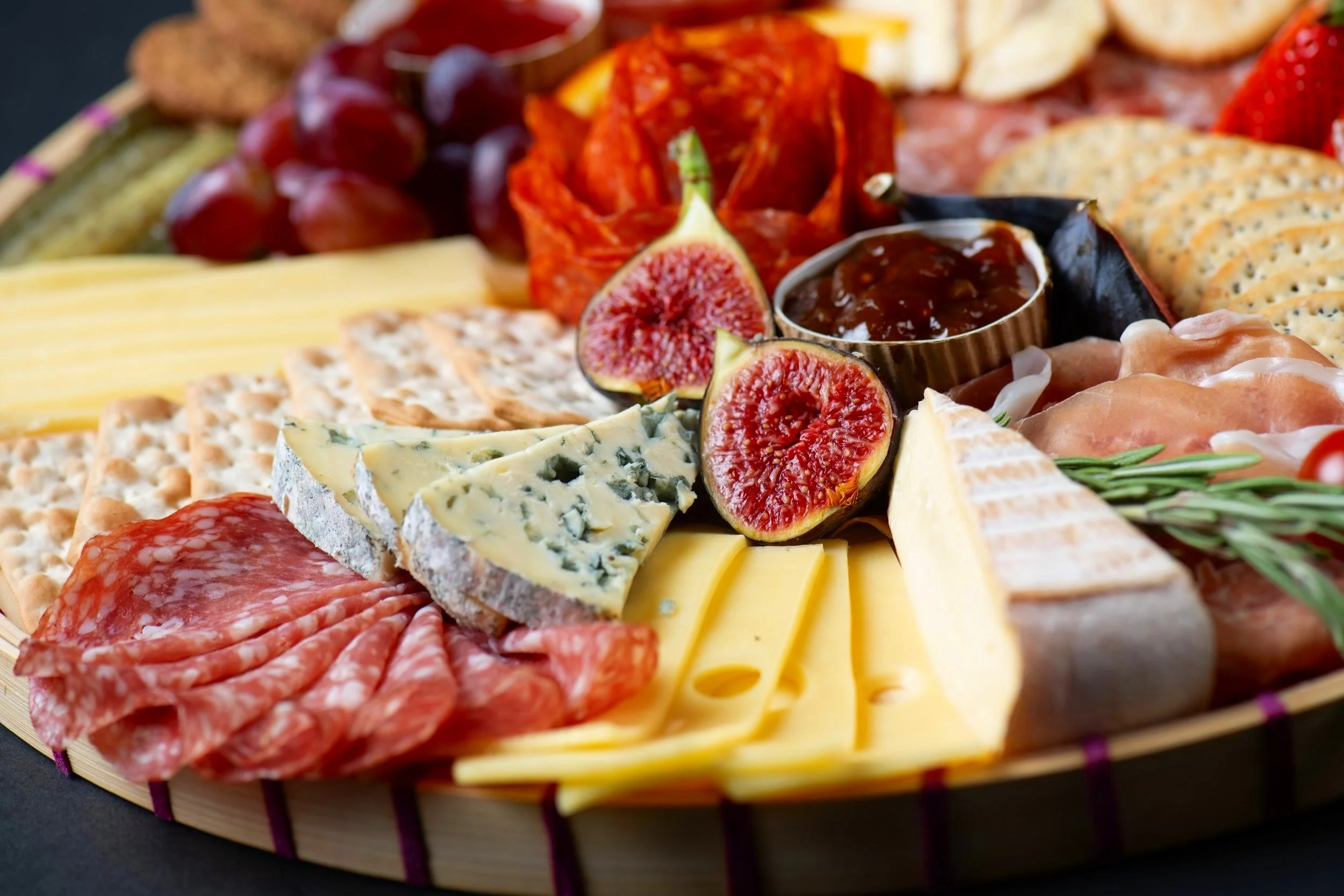 Assorted charcuterie board with various cheeses, sliced meats, figs, crackers, grapes, and a small dish of jam.