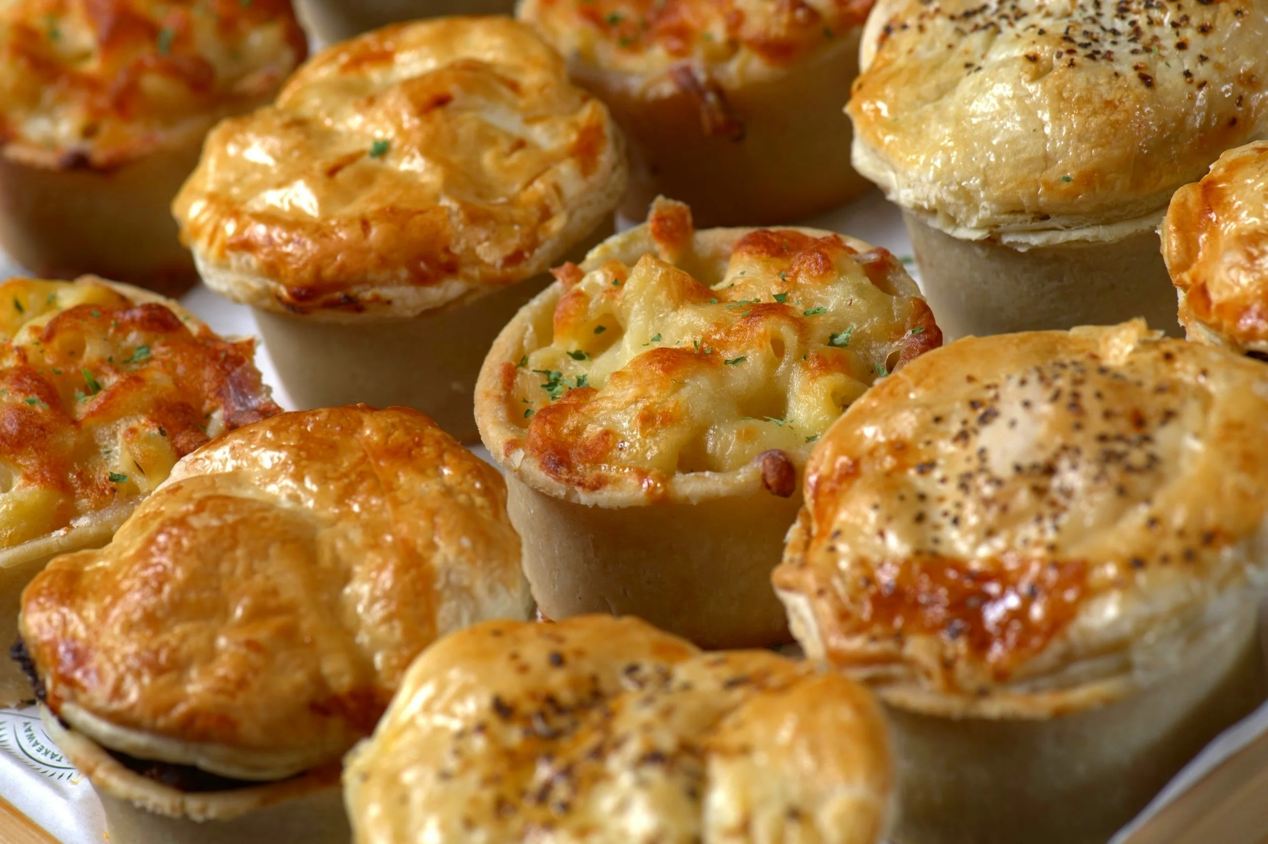 Assorted mini savory pies with golden crusts, some with cheese toppings.