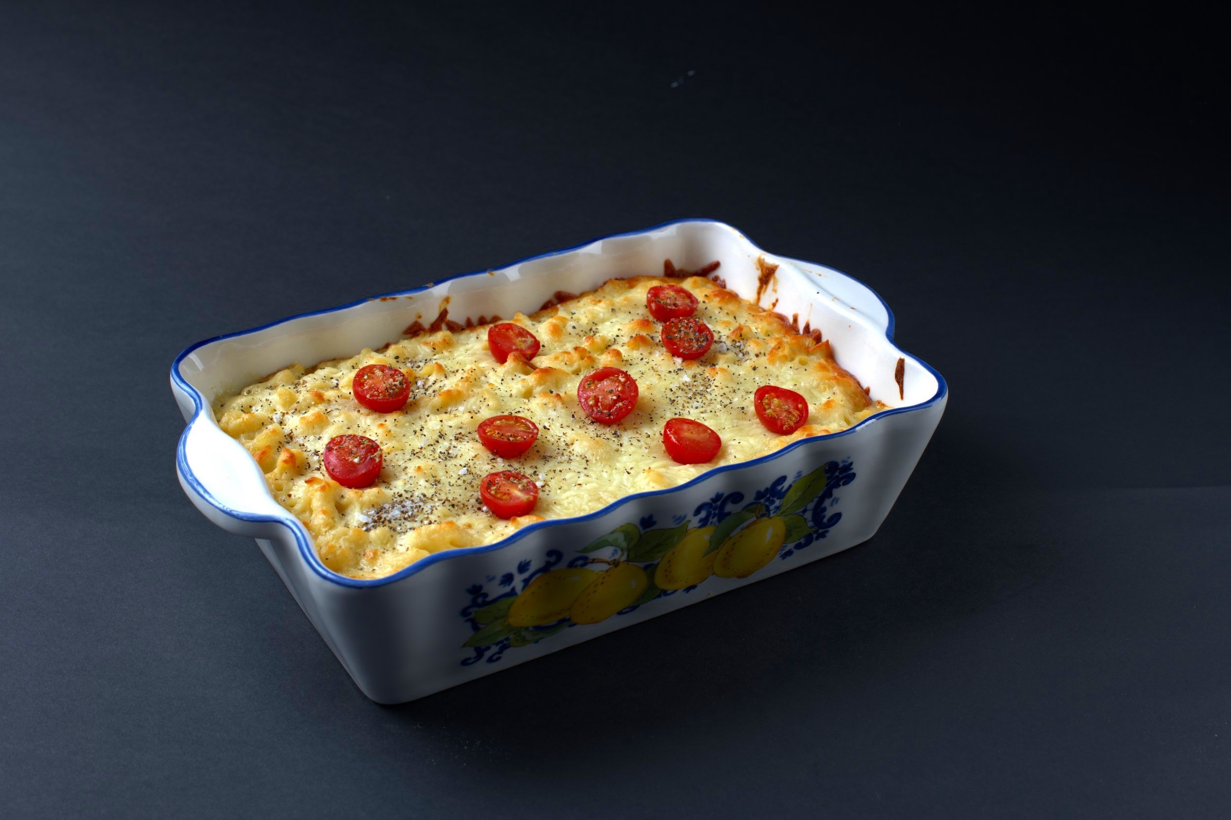 Baked macaroni and cheese with cherry tomatoes in a decorative dish.