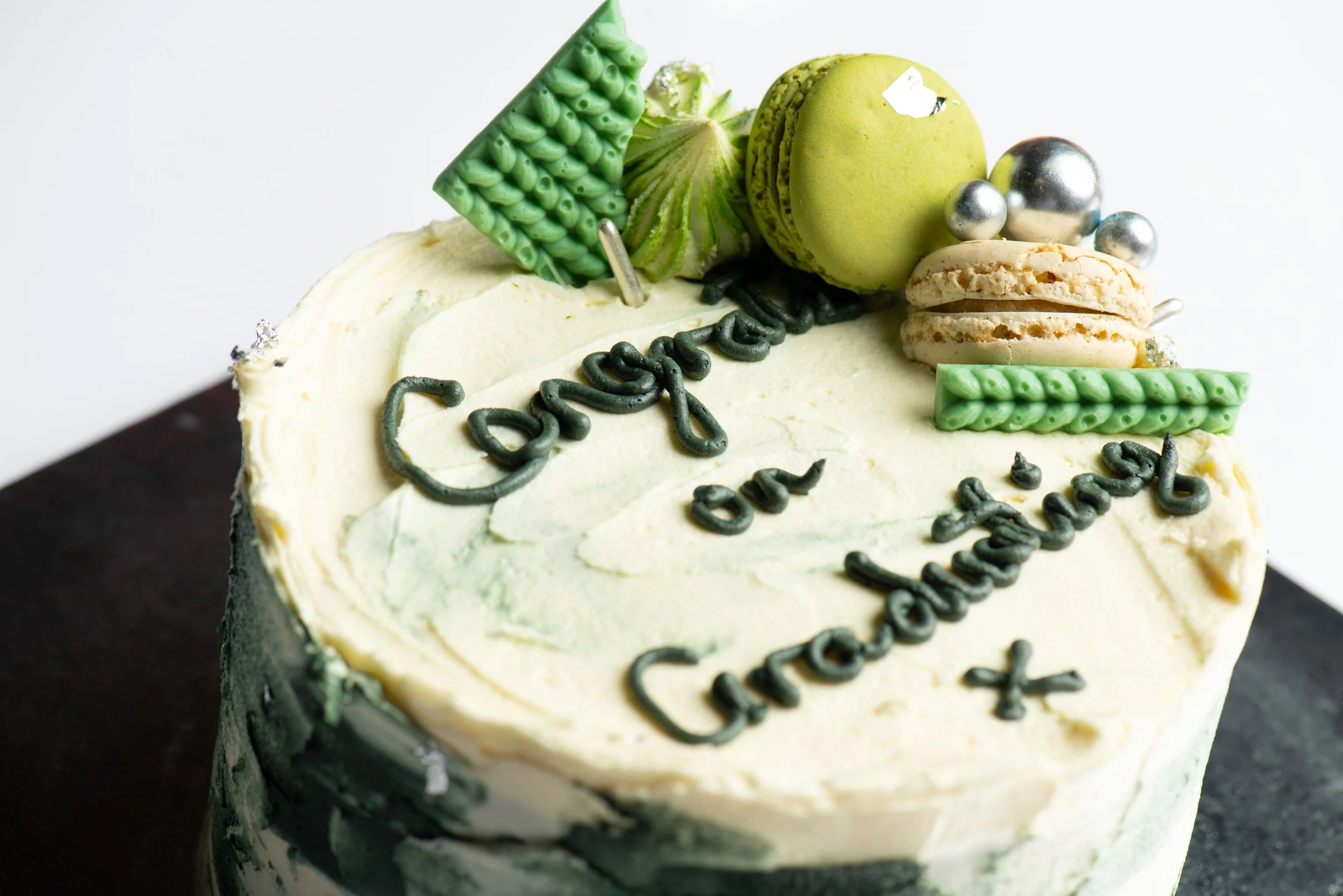 Graduation cake with green decorations, macarons, and "Congrats on Graduating" written in frosting.