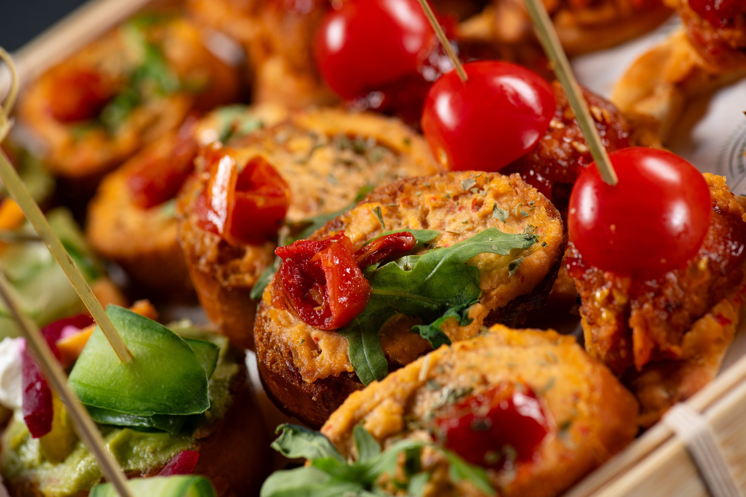 Close-up of assorted gourmet appetizers with cherry tomatoes, herbs, and greens on a wooden tray.