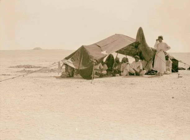 People sitting under a makeshift shelter in a desert landscape.