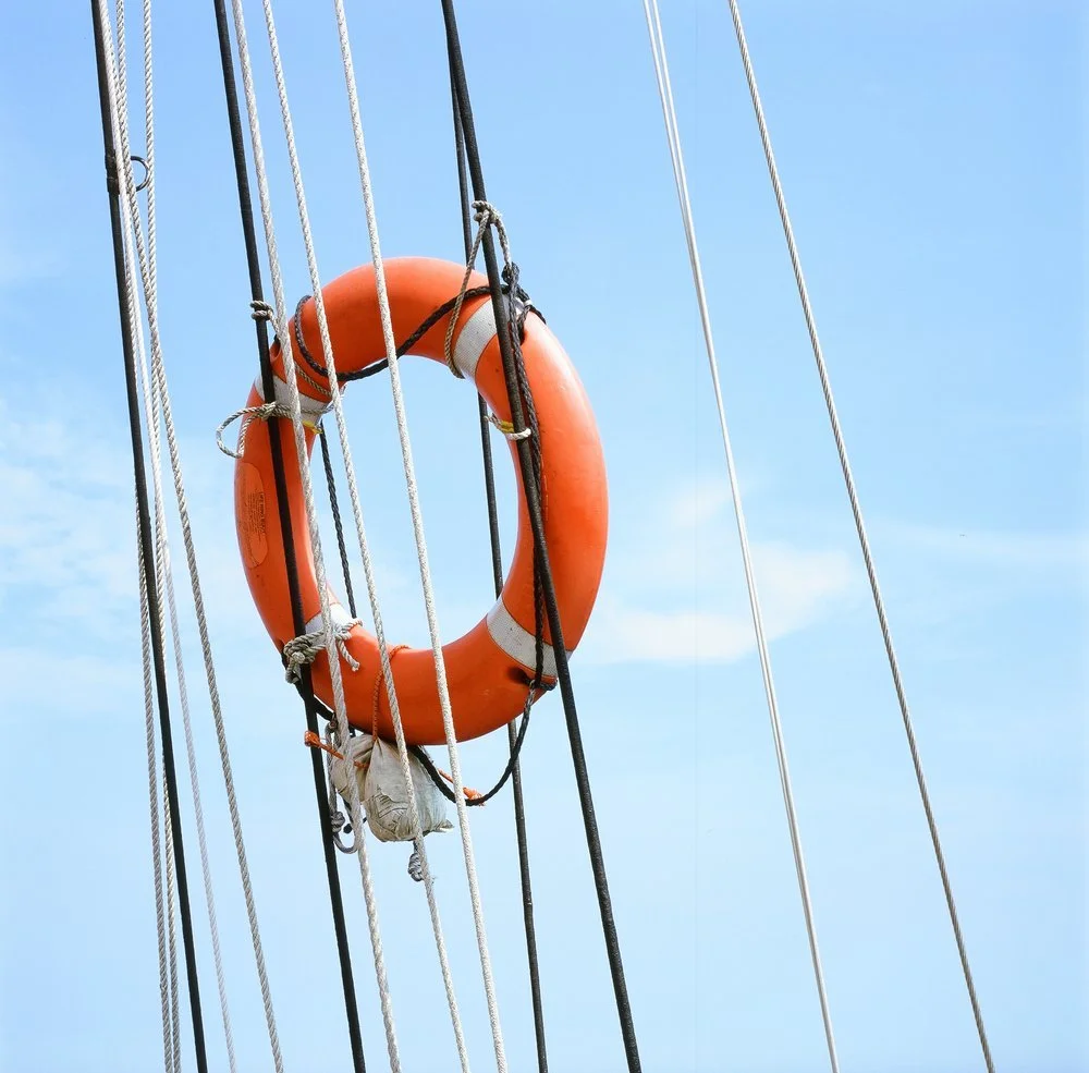 An orange lifebuoy hanging on a ship's rigging with a clear blue sky in the background.