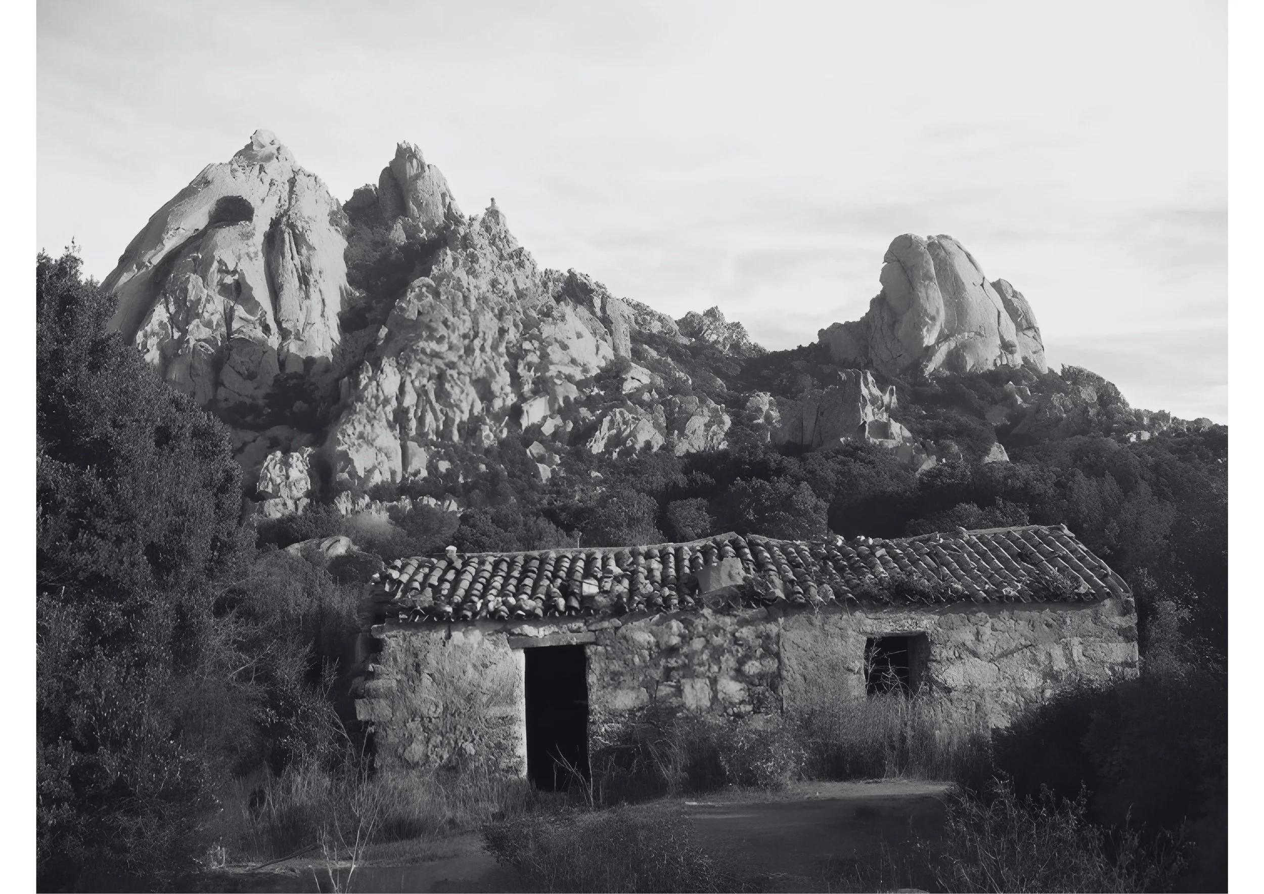 Old stone house with cracked roof tiles in front of rugged mountains and trees