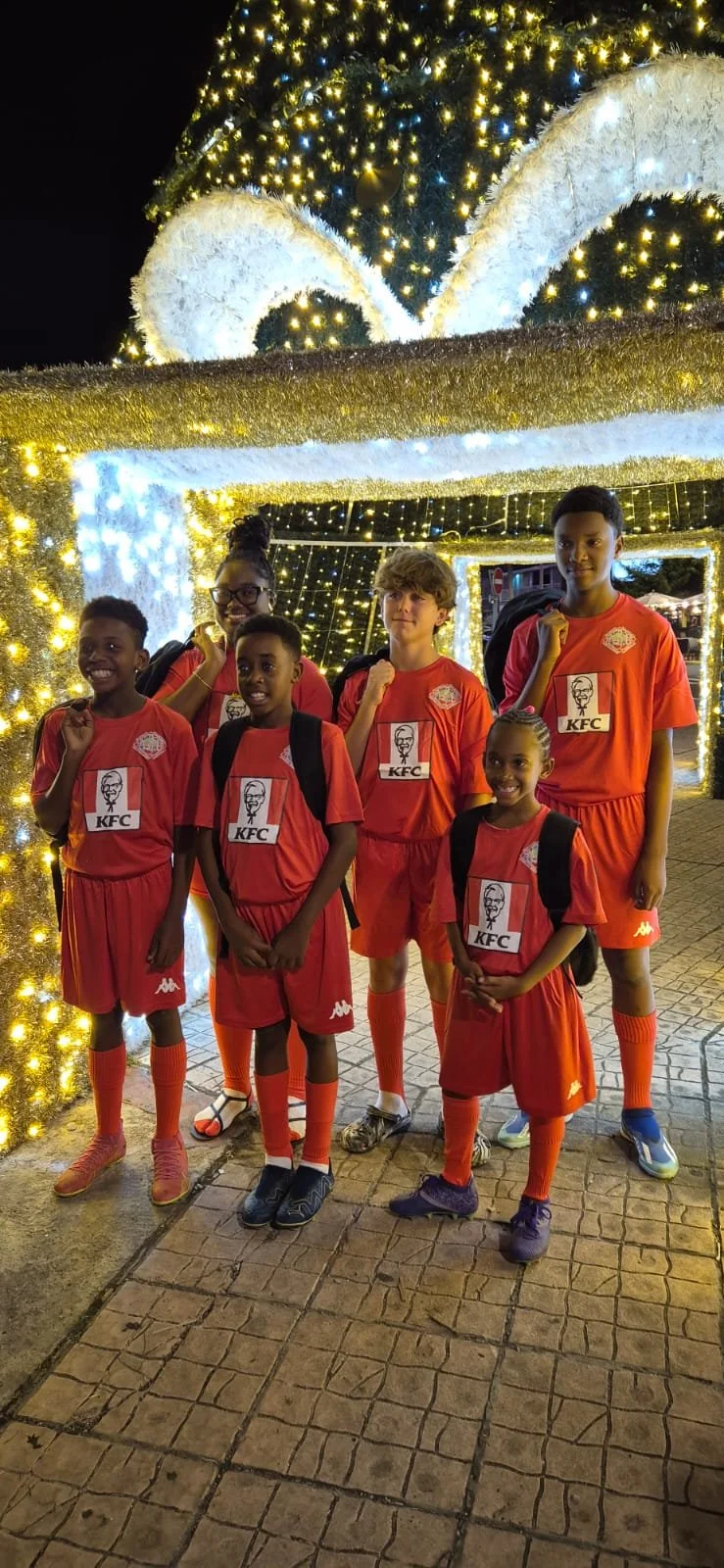 Groupe de jeunes enfants en tenue de football rouge, posant devant une décoration de Noël illuminée.