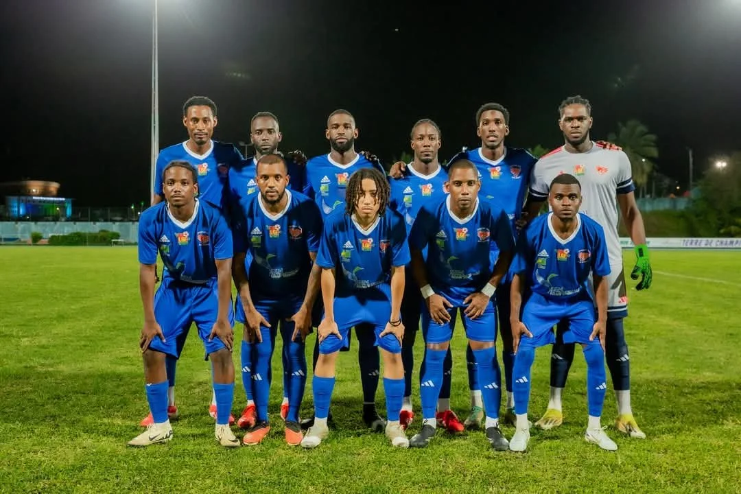 Équipe de football posant sur un terrain éclairé la nuit, portant des maillots bleus avec un gardien en gris
