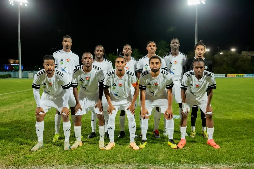 Équipe de football en tenue blanche, posant sur un terrain de nuit, éclairé par des projecteurs.