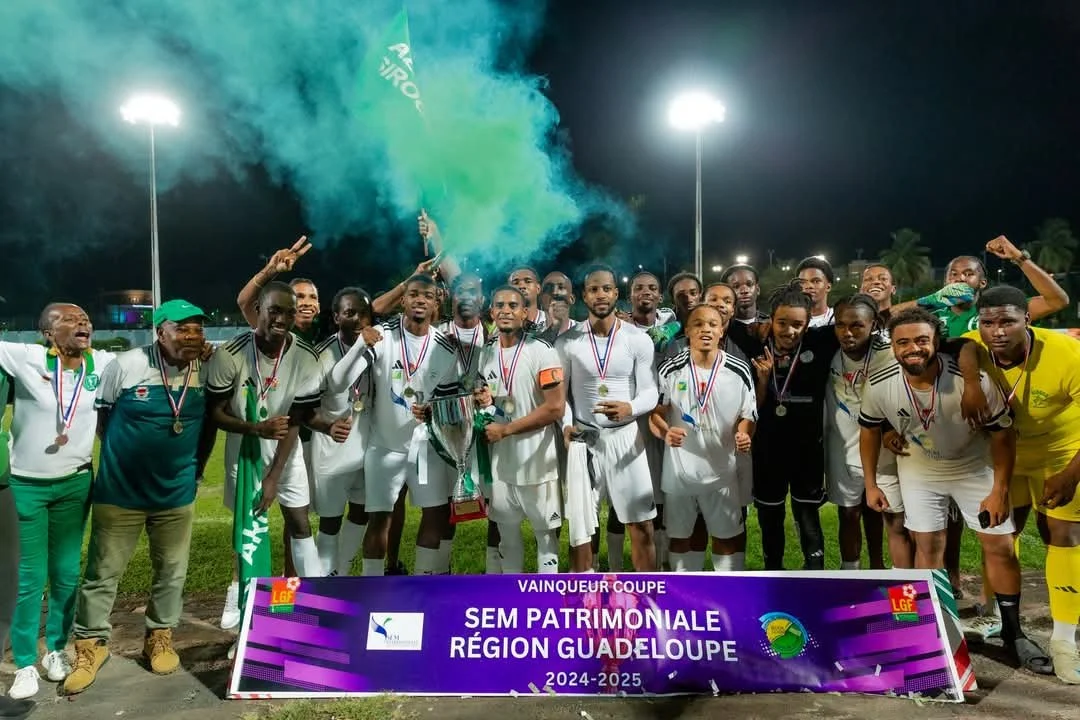 Une équipe de football célébrant leur victoire lors d'une cérémonie nocturne, avec des médailles, un trophée et un drapeau, sous des lumières de stade et de la fumée colorée en arrière-plan.