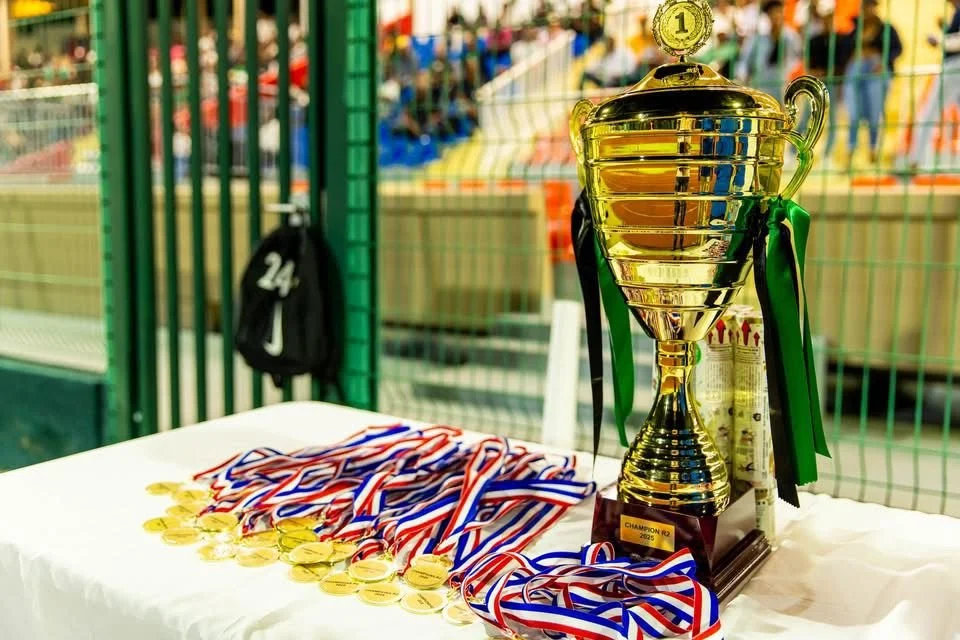 Trophée de championnat en or avec rubans verts, entouré de médailles en or portant des rubans rouges, blancs et bleus."