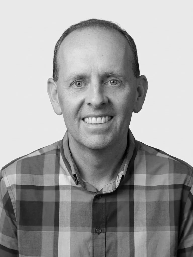 Black and white portrait of a smiling man wearing a checkered shirt.